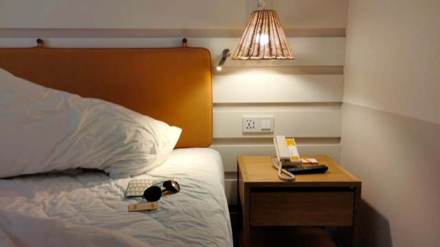 Hotel room bed beside a lamp-lit nightstand